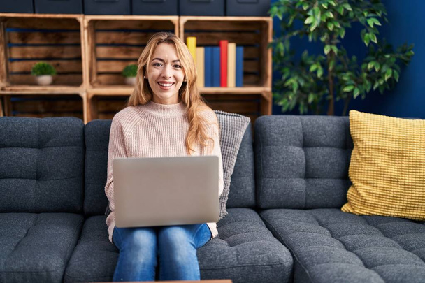 Young woman using laptop sitting on sofa at home - Фото, изображение