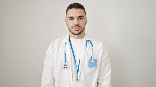 Joven médico hispano de pie con expresión seria sobre fondo blanco aislado - Foto, Imagen