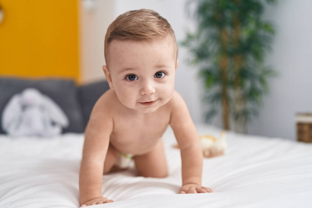 Imádnivaló kaukázusi baba mászik az ágyon a hálószobában - Fotó, kép
