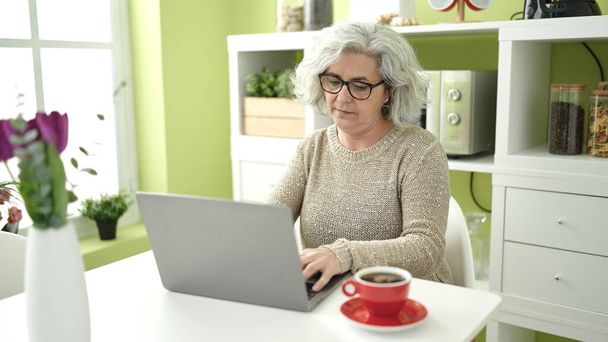 Middle age woman with grey hair using laptop sitting on table at home - Fotografie, Obrázek