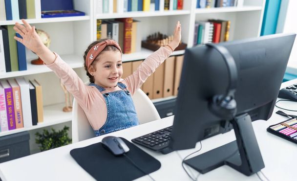 Adorable hispanic girl student using computer with winner expression at classroom - Photo, Image