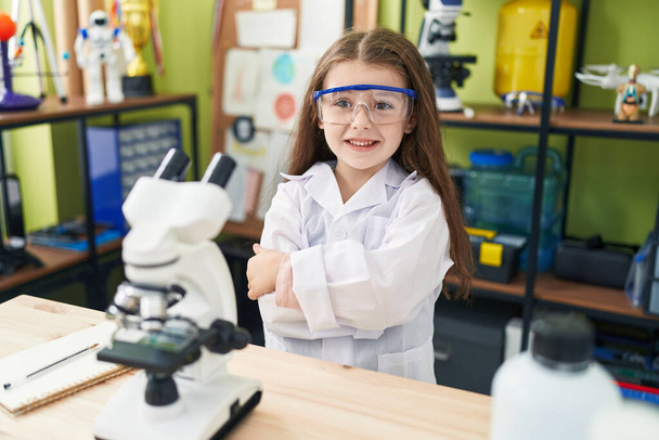 Adorable estudiante hispana sonriendo confiada de pie con los brazos cruzados gesto en el aula de laboratorio - Foto, Imagen