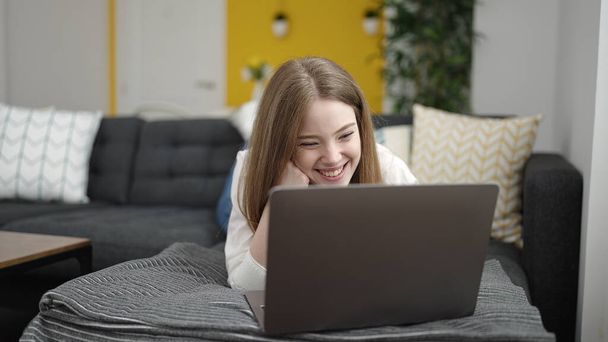 Young blonde woman using laptop lying on sofa at home - Foto, Imagem