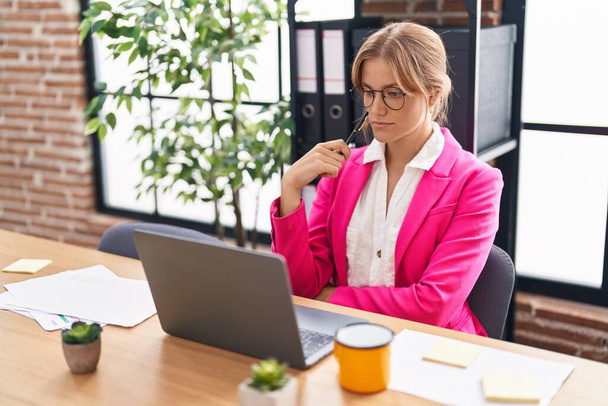 Молодая блондинка бизнес-работница с помощью ноутбука с сомнением выражение в офисе - Фото, изображение