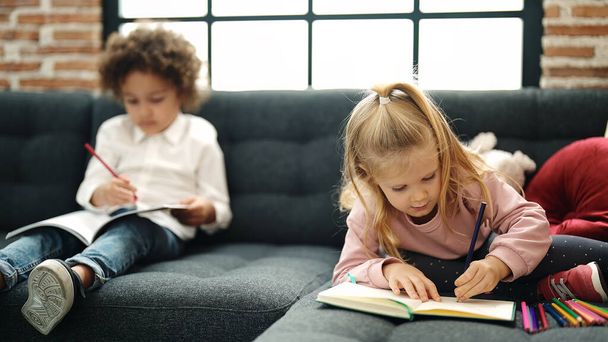 Adorable boy and girl students sitting on sofa drawing on notebook at home - Photo, Image