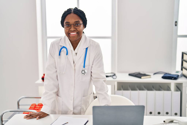 Africano americano mulher médico sorrindo confiante por mesa na clínica - Foto, Imagem