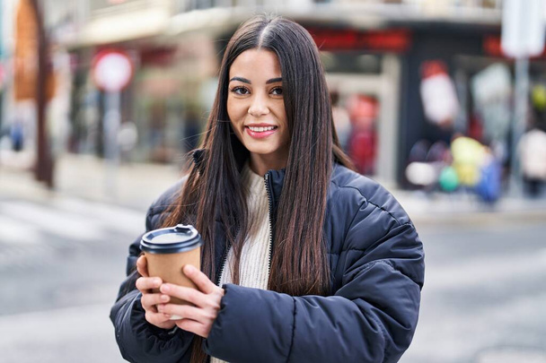 Young beautiful hispanic woman smiling confident drinking coffee at street - Valokuva, kuva