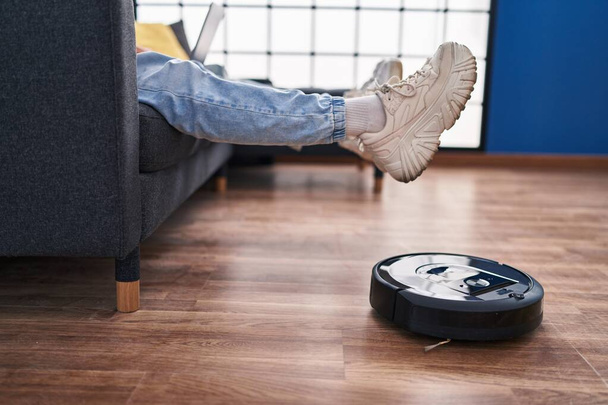 Two man couple using laptop and vacuum cleaner robot sitting on sofa at home - Foto, Imagem