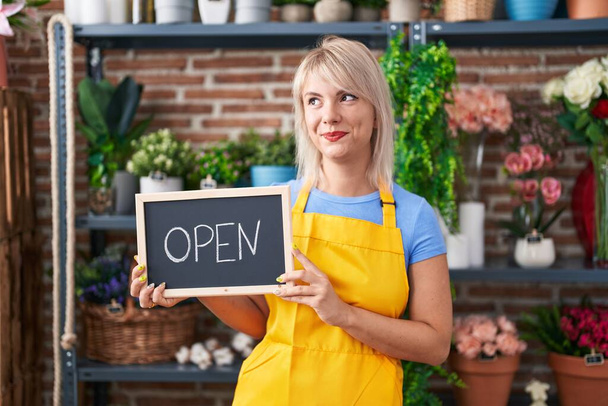 Young caucasian woman working at florist holding open sign smiling looking to the side and staring away thinking.  - Photo, Image
