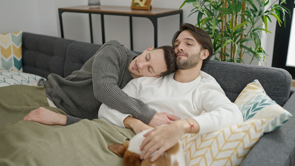 Dos hombres pareja abrazándose uno al otro relajándose en el sofá con perro en casa - Foto, imagen