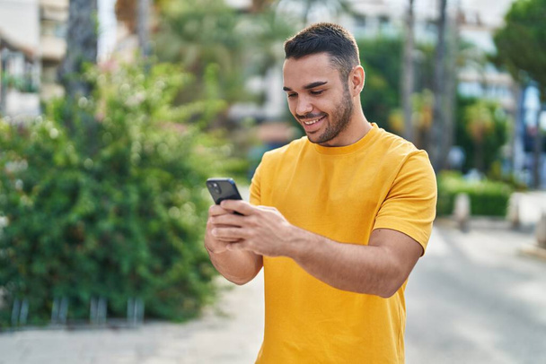 Young hispanic man smiling confident using smartphone at street - Foto, imagen