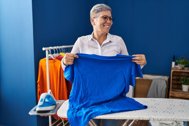 Middle age woman smiling confident ironing clothes at laundry room - Valokuva, kuva