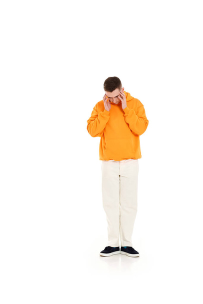 thoughtful man in orange sweatshirt holding arms near head on white background - Photo, Image