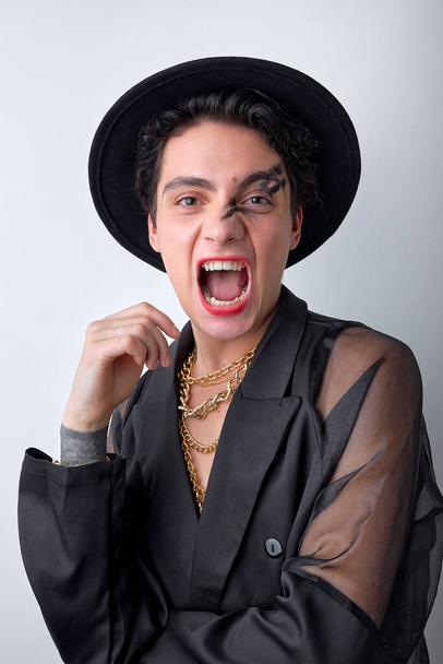 emotive excited gender 20s transgender gay man wearing necklace and hat, isolated on white background. handsome happy gay looking at camera screaming, with wide opened mouth. portrait - Photo, Image