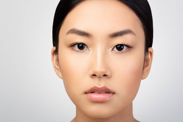 Pura belleza. Primer plano de la cara de las mujeres jóvenes asiáticas con maquillaje natural y emociones genuinas calma sobre fondo gris claro del estudio. Retrato de la atractiva mujer coreana. Cultivado - Foto, imagen