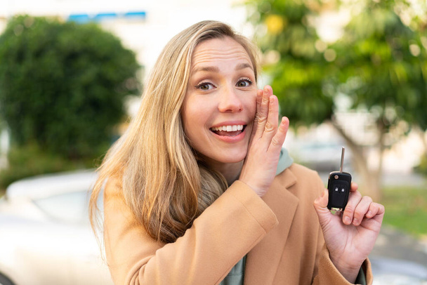Jeune femme blonde tenant des clés de voiture à l'extérieur chuchotant quelque chose - Photo, image