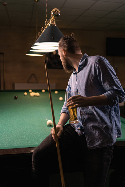 Millennial-Mann amüsiert sich in einer Nacht in einem Billardclub und trinkt Bier. Billardsportkonzept. - Foto, Bild