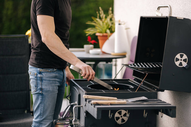 Handsome man make a fire and controls the process. BBQ grill outdoor. High quality photo - Valokuva, kuva