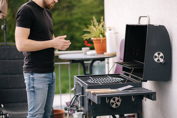 Handsome man cleaning BBQ grill to make some steak. Male use napkin to clean the grill of grease. High quality photo - Photo, Image