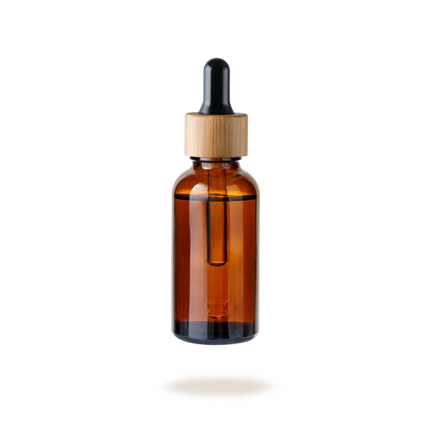Glass dropper bottle with cap of bamboo wood for face serum or essential oil or pharmaceutical tincture. Glass and wooden bottle flying isolated on white background. Zero waste concept. - Photo, Image