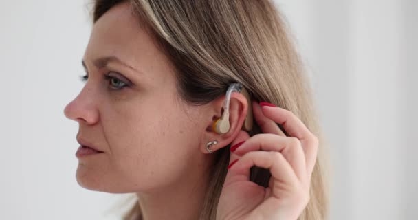 El audífono está en el oído de la mujer y ajusta el sonido. Elegir audífonos de calidad - Imágenes, Vídeo