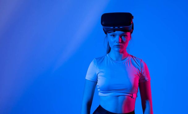 Junge brünette Frau trägt Virtual-Reality-Gerät, Vr-Brille und spielt ein Spiel mit Freunden online in Neonlicht - Foto, Bild