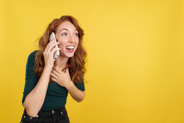 Kızıl saçlı kadın, sarı arka planlı cep telefonuyla stüdyoda iyi haberler alıyor. - Fotoğraf, Görsel