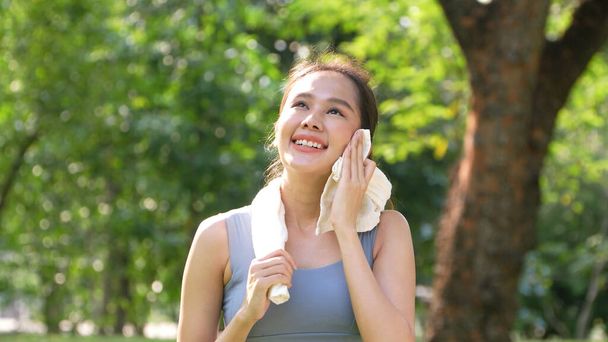 Retrato joven mujer asiática atractiva sonriendo y el uso de toalla blanca descansando después del entrenamiento. Sonriente joven deportista haciendo ejercicio al aire libre y mirando a la cámara. Vida sana bienestar bienestar - Foto, imagen