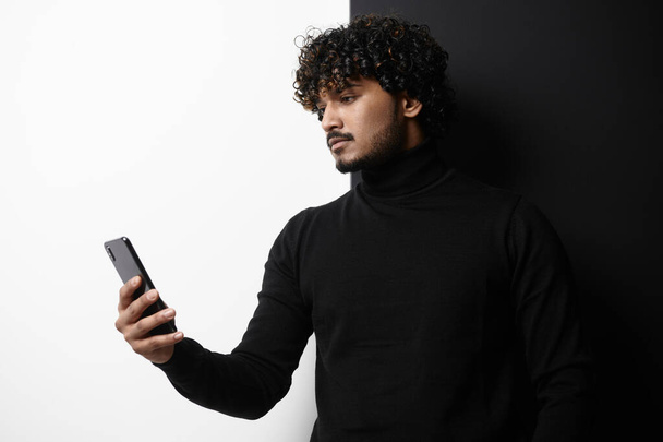 Handsome Indian man using smart phone while standing against black and white background - Fotó, kép