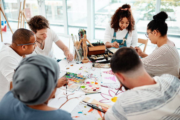 Językiem przyjaciół nie są słowa, ale znaczenia. zróżnicowana grupa artystów siedzących razem i malujących podczas zajęć plastycznych w studiu - Zdjęcie, obraz