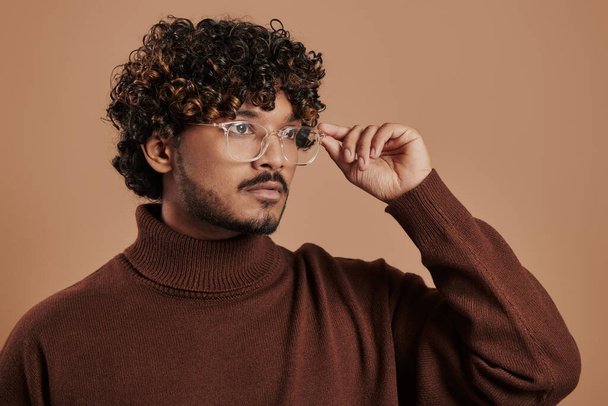 Πορτρέτο του όμορφου Ινδού ρυθμίζοντας γυαλιά με φόντο καφέ - Φωτογραφία, εικόνα