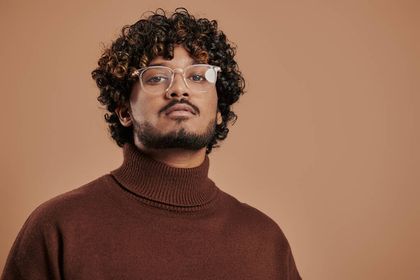 Portrait of handsome Indian man in eyeglasses looking at camera against brown background - Foto, immagini