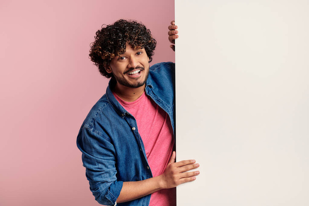 Happy young Indian man leaning on the copy space while standing against pink background - Zdjęcie, obraz