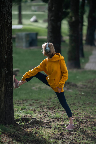 A woman wearing headphones warms-up up in the park. - Foto, Imagen