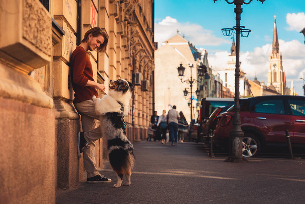 Side view of young Caucasian man with pure breed aussie dog poses leans wall. Background of city. Friendship with pet. - Valokuva, kuva