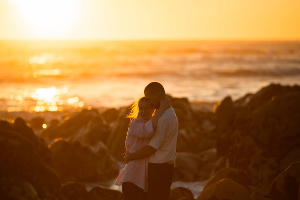 Una pareja joven en una cita romántica junto al océano durante una encantadora puesta de sol.  - Foto, imagen