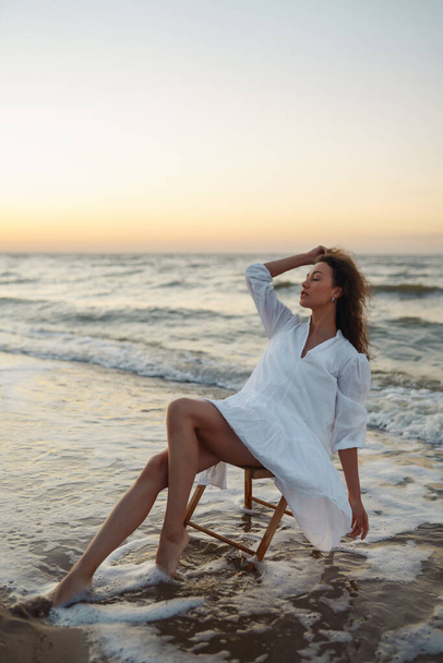 Young woman enjoys an incredible sunrise on the beach. Fashion, style concept. People, lifestyle, relaxation and vacations concept. - Photo, image