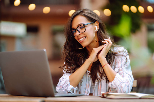 Young woman with wireless headphones calling on laptop, talk by webcam, video conference sitting on modern cafe. Concept for education, business, blog or freelance. - Φωτογραφία, εικόνα