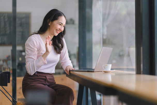 Женщина-предприниматель машет рукой во время видеозвонка на ноутбуке в офисе - Фото, изображение