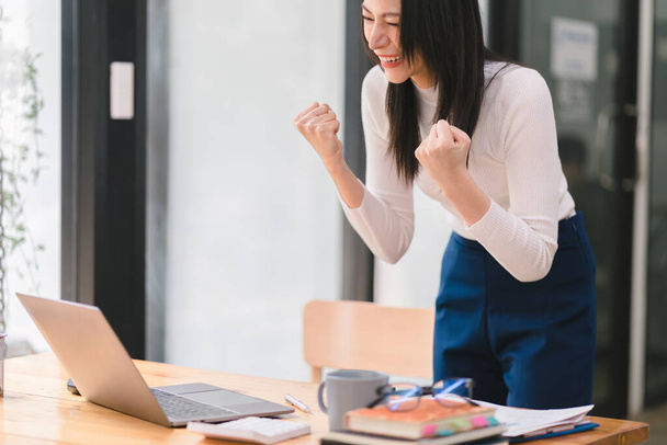 Happy and excited, a young asian woman student or office worker, celebrates achieving her goal of winning an online competition or receiving good news via email by raising hands in euphoria - Foto, imagen