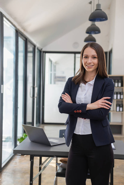 A stylish white businesswoman in a black suit standing inside the office in hands with a mobile phone, tablet, and laptop waiting for customers to contact, business people concept. - Foto, afbeelding