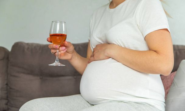 Eine schwangere Frau trinkt Wein in einem Glas. Selektiver Fokus. Lebensmittel. - Foto, Bild