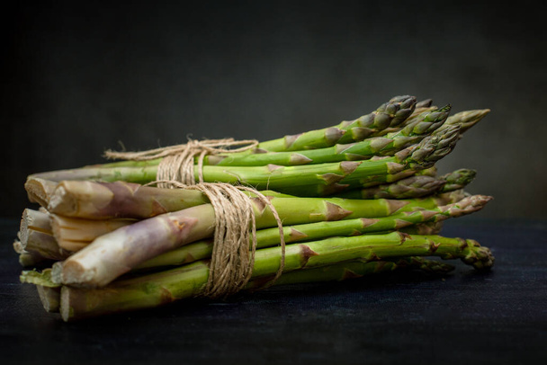 Green asparagus in a bunch. Vegetable season. May delicacies. Healthy food. Vegan delicacies. Dark background. - Foto, imagen
