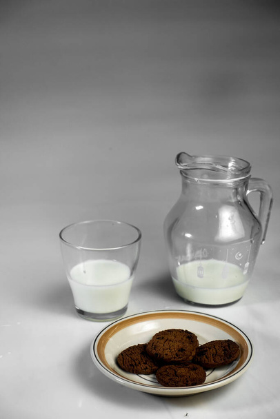 Concept de fond pour la journée mondiale du lait, image une cruche de verre de lait et des biscuits sur la table, isolé en arrière-plan blanc, espace de copie. - Photo, image