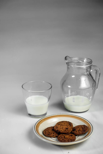 Concept de fond pour la journée mondiale du lait, image une cruche de verre de lait et des biscuits sur la table, isolé en arrière-plan blanc, espace de copie - Photo, image