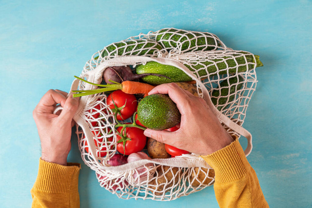 Homme prenant à la main les fruits de pêche du sac à provisions en maille avec des fruits et légumes. Des achats écologiques. Style de vie durable, zéro déchet, concept sans plastique - Photo, image