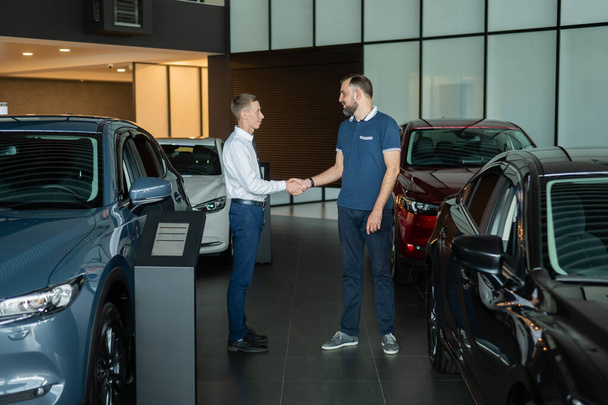 Seller and buyer shake hands in a car dealership. Caucasian man buys a car - Фото, изображение