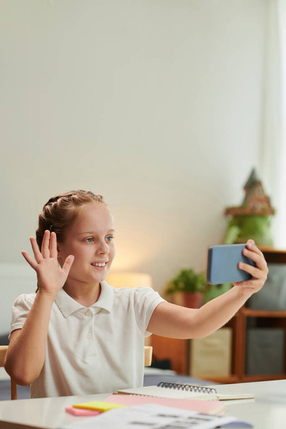 Cheerful preteen girl video calling friend to discuss homework - Foto, immagini
