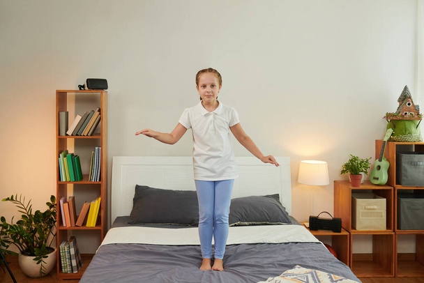 Chica alegre saltando en la cama, divirtiéndose en casa después de la escuela - Foto, Imagen