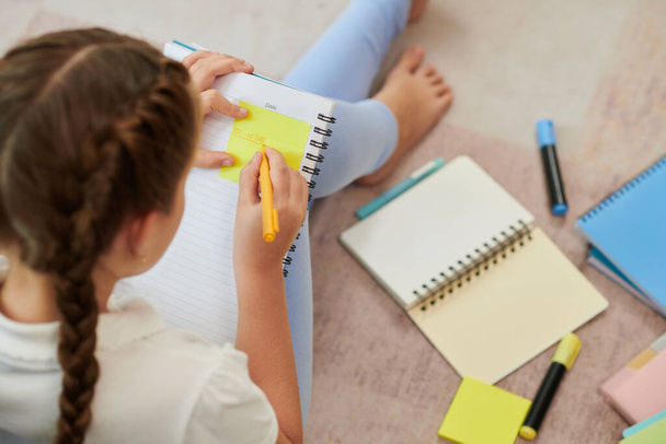 Schoolmeisje schrijven belangrijke informatie over gele stickers bij de voorbereiding van de school examens thuis - Foto, afbeelding